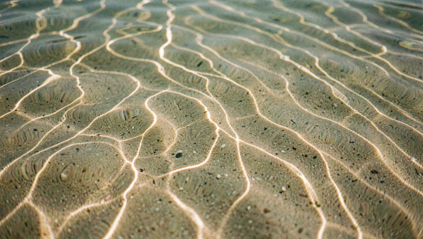 Eau très claire sur un fond de sable ondulé, la lumière verticale dessine un réseau de lignes mouvantes
