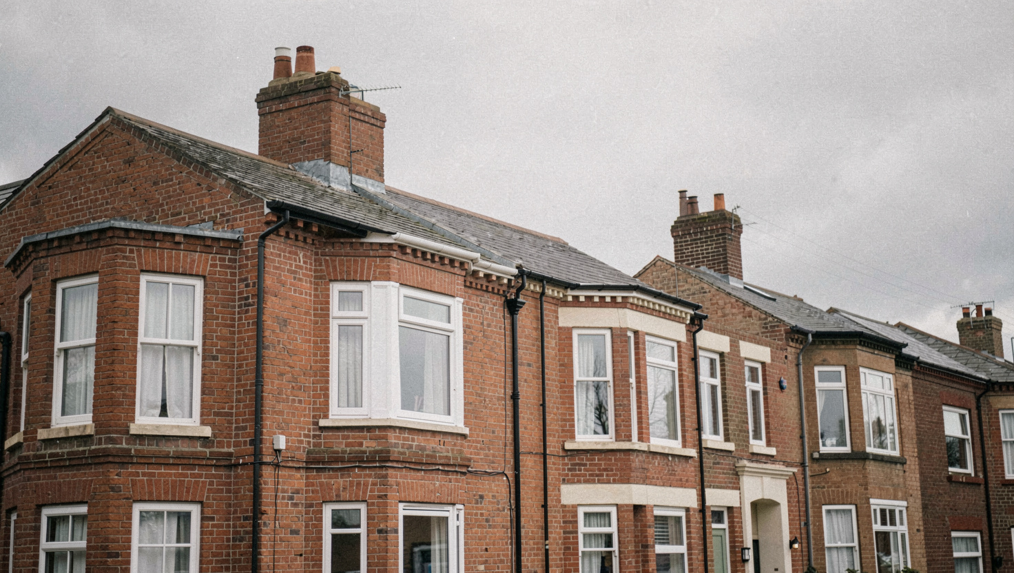 Alignement de maisons de brique rouge à bow-windows sous un ciel gris uniforme, la couleur de la brique ressort sans aucune ombre portée